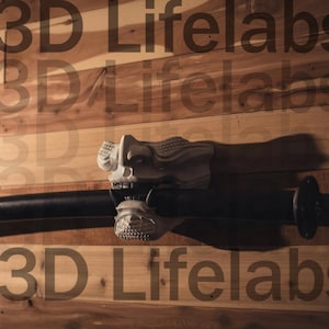 May include: A white 3D printed mask with a samurai design is mounted on a black katana sword. The sword is mounted on a wooden wall with the text "3D Lifelabs" repeated multiple times.
