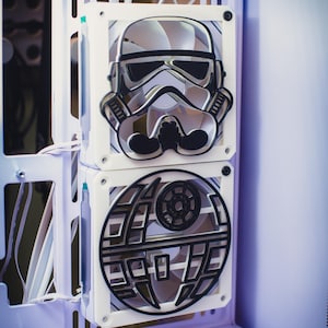 以下が含まれることがあります： 白いコンピューターケースに2つのカスタムファン。 上部のファンはストームトルーパーのヘルメットのデザインで、下部のファンはデススターのグラフィックです。 両方のファンは白と黒のディテールがあり、ケース内に取り付けられています。