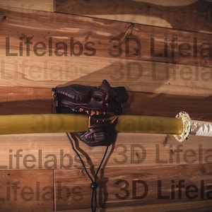 May include: A katana sword with a yellow blade and white handle, mounted on a wooden wall. The sword is held in place by a dark brown decorative piece. The text "3D Lifelabs" is faintly visible.