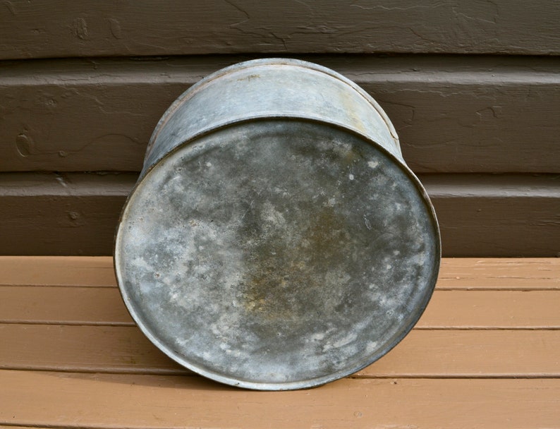 May include: A vintage galvanised metal bucket with a worn, weathered surface. The bucket is round and has a slightly dented bottom.