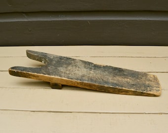 May include: An antique wooden boot jack with a dark, weathered finish. The boot jack is a long, flat piece of wood with a forked end and a small support piece on the bottom. The wood has a distressed look.