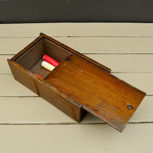 May include: A wooden box with a hinged lid, open to reveal three red and white crayons inside.