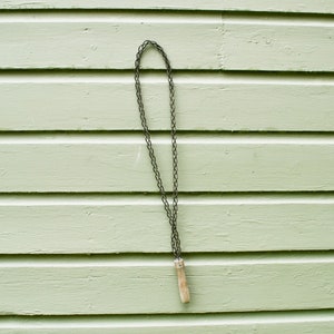 May include: A chain saw sharpener with a wooden handle hanging on a light green wooden wall.