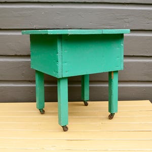 K&ouml;nnte beinhalten: Ein t&uuml;rkisfarbener Holztisch mit vier Beinen und Rollen. Der Tisch hat eine rechteckige Tischplatte und ist aus Holz.