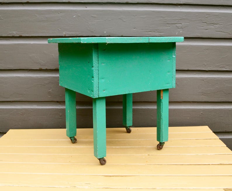 K&ouml;nnte beinhalten: Ein t&uuml;rkisfarbener Holztisch mit vier Beinen und Rollen. Der Tisch hat eine rechteckige Tischplatte und ist aus Holz.