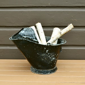 May include: A black metal coal scuttle with a handle, filled with white birch logs.