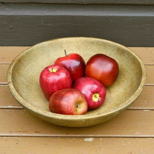May include: Five red apples in a wooden bowl. The bowl is light brown and has a smooth surface. The apples are arranged in a circle, with the stems facing up.