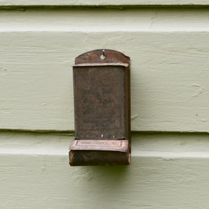 May include: A rusty metal matchbox holder attached to a light green wooden wall.