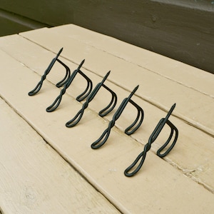 May include: A set of six black metal screw-in hooks. Each hook has a twisted design and a curved bottom, ideal for hanging items. The hooks are arranged diagonally on a light-colored wooden surface.