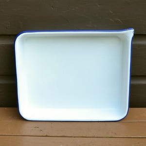 May include: A white enamel baking pan with a blue rim. The pan is rectangular and has a slight lip around the edge.