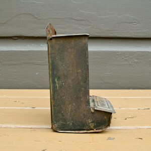 May include: A vintage metal bird feeder with a rusty green finish. The feeder has a small opening on the front and a slanted bottom.