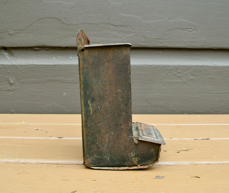 May include: A vintage metal bird feeder with a rusty green finish. The feeder has a small opening on the front and a slanted bottom.