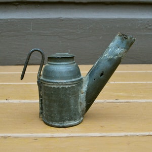 May include: A vintage, green metal oil lamp with a long spout and a handle. The lamp has a worn, aged appearance.