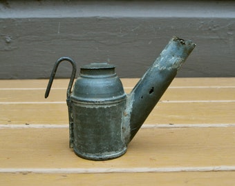 May include: A vintage, green metal oil lamp with a long spout and a handle. The lamp has a worn, aged appearance.
