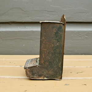 May include: A vintage metal bird feeder with a rusty green finish. The feeder has a small opening at the bottom for birds to access the seeds.