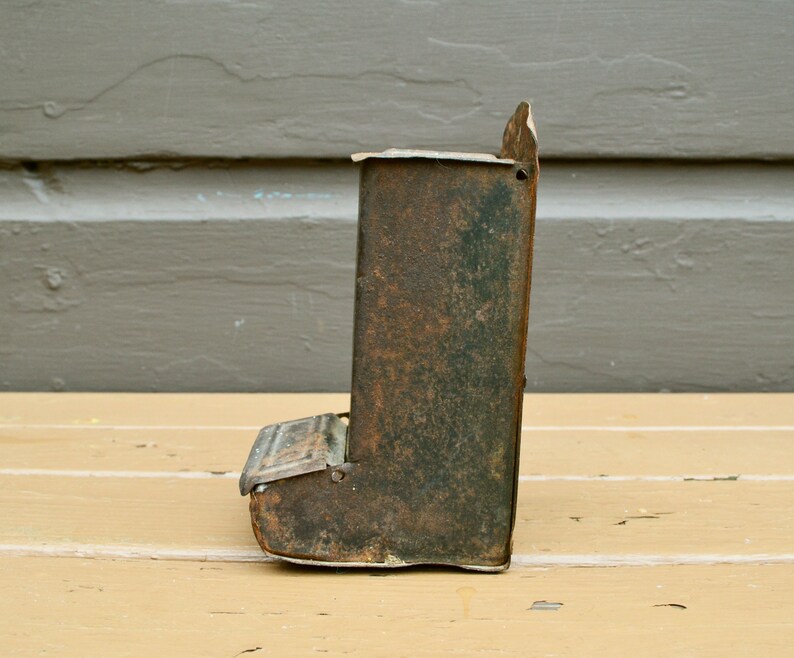 May include: A vintage metal bird feeder with a rusty green finish. The feeder has a small opening at the bottom for birds to access the seeds.
