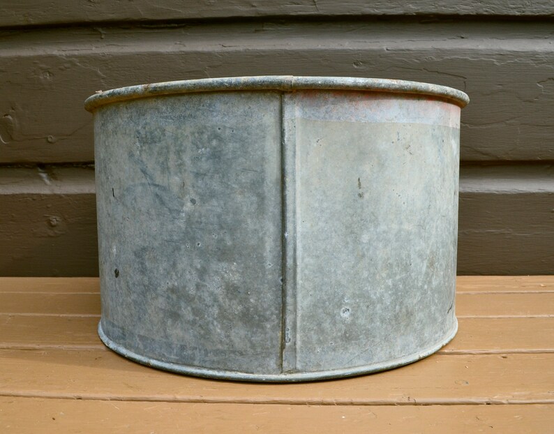 May include: A large, round, galvanised metal planter with a slightly distressed finish. The planter is empty and has a slightly rounded bottom.