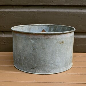 May include: A vintage galvanised metal planter with a slightly rounded top and a worn, rustic finish.