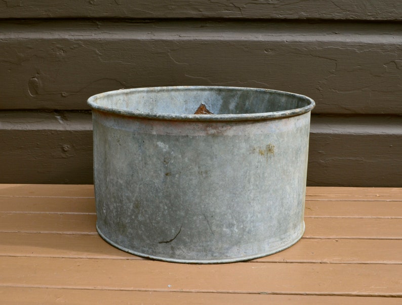 May include: A vintage galvanised metal planter with a slightly rounded top and a worn, rustic finish.