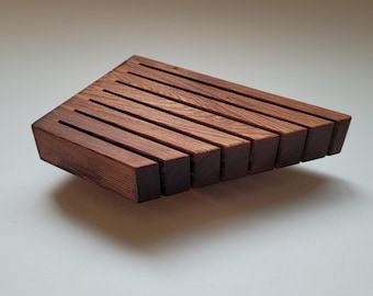May include: A trapezoidal wooden knife block featuring a series of parallel vertical slots for storage. The object is crafted from dark brown wood with a visible grain pattern, showcasing a clean, angular design with eight distinct wooden slats.
