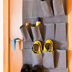 May include: A gray fabric over-the-door shoe organizer with 12 pockets. The organizer is filled with various shoes, including flip-flops, sneakers, and sandals.