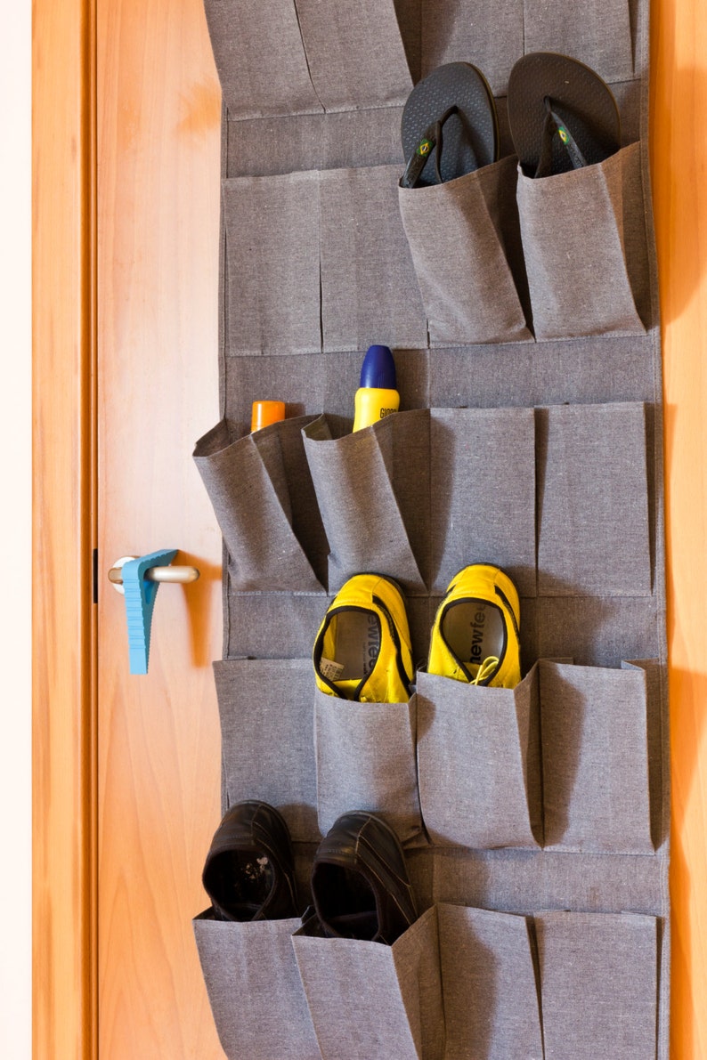 May include: A gray fabric over-the-door shoe organizer with 12 pockets. The organizer is filled with various shoes, including flip-flops, sneakers, and sandals.