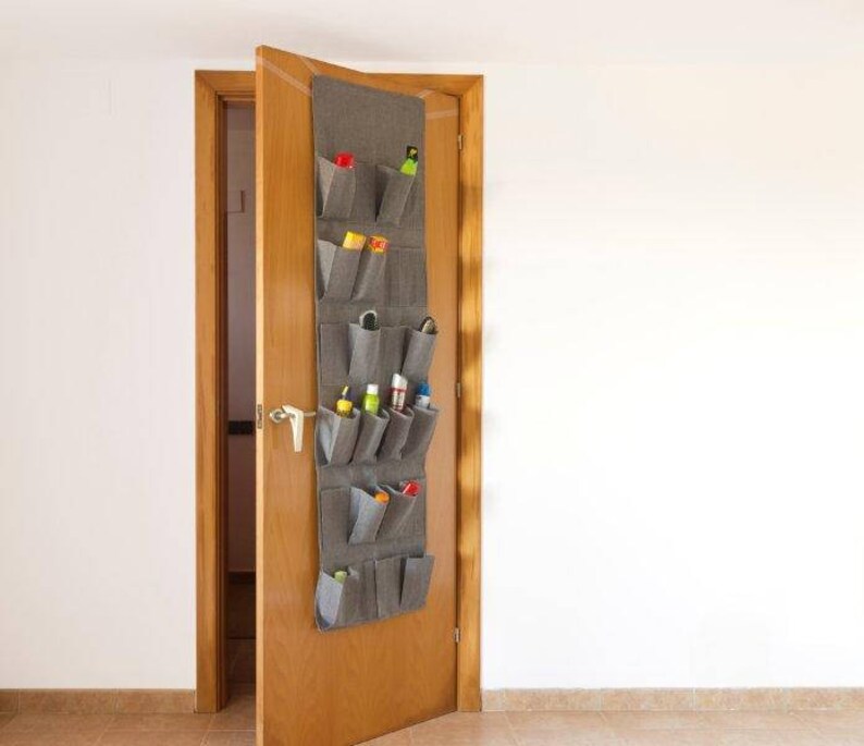 May include: A gray fabric over-the-door shoe organizer with 10 pockets. The organizer is hanging on a wooden door and is filled with various items, including shoes, cleaning supplies, and other household items.