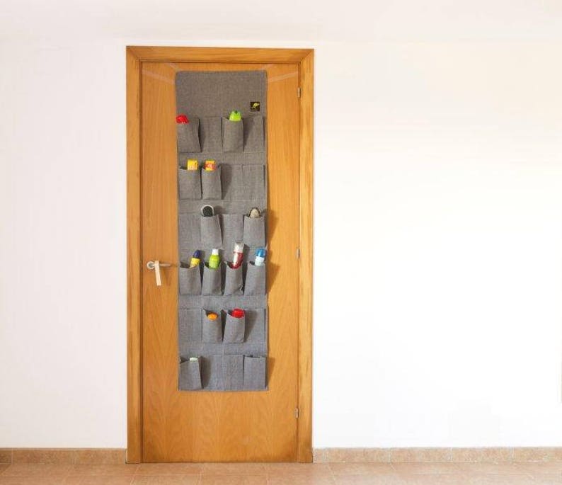 May include: A gray felt over-the-door shoe organizer with 16 pockets. The organizer is hanging on a wooden door and is filled with various items, including bottles of cleaning supplies and other household items.