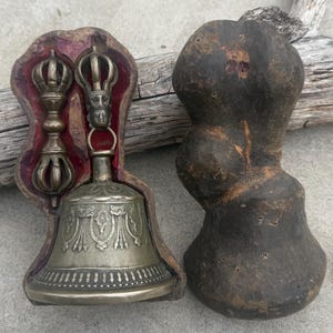 May include: A silver bell with intricate designs and two silver hand-held prayer wheels, all in a wooden box with a red velvet lining.