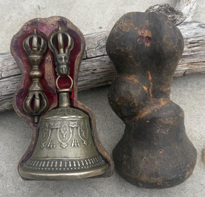 May include: A silver bell with intricate designs and two silver hand-held prayer wheels, all in a wooden box with a red velvet lining.