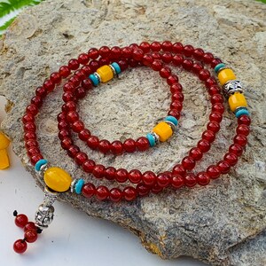 May include: A red and yellow beaded necklace with silver accents. The necklace is made of small, round beads and has a tassel at the end.