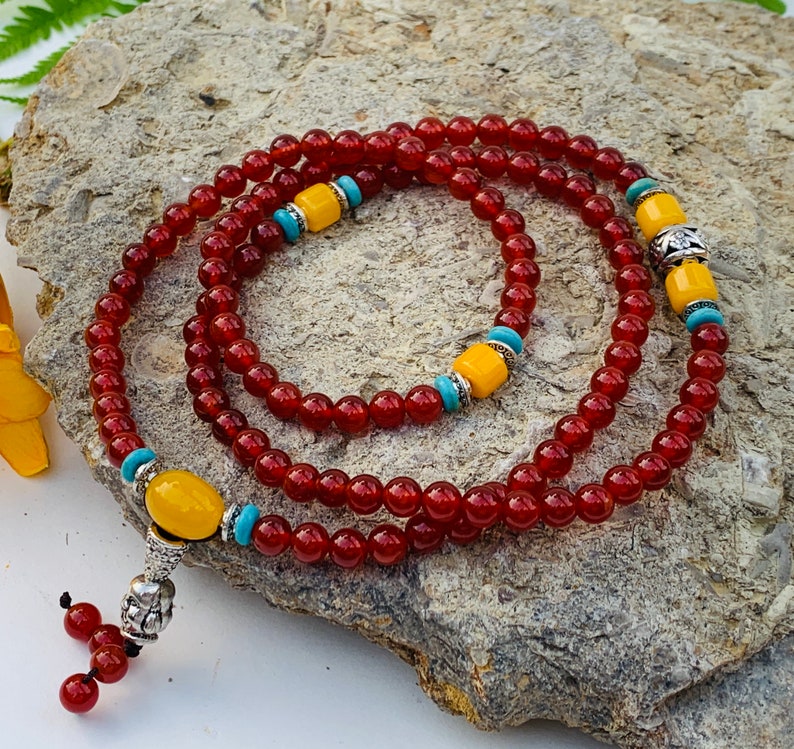 May include: A red and yellow beaded necklace with silver accents. The necklace is made of small, round beads and has a tassel at the end.