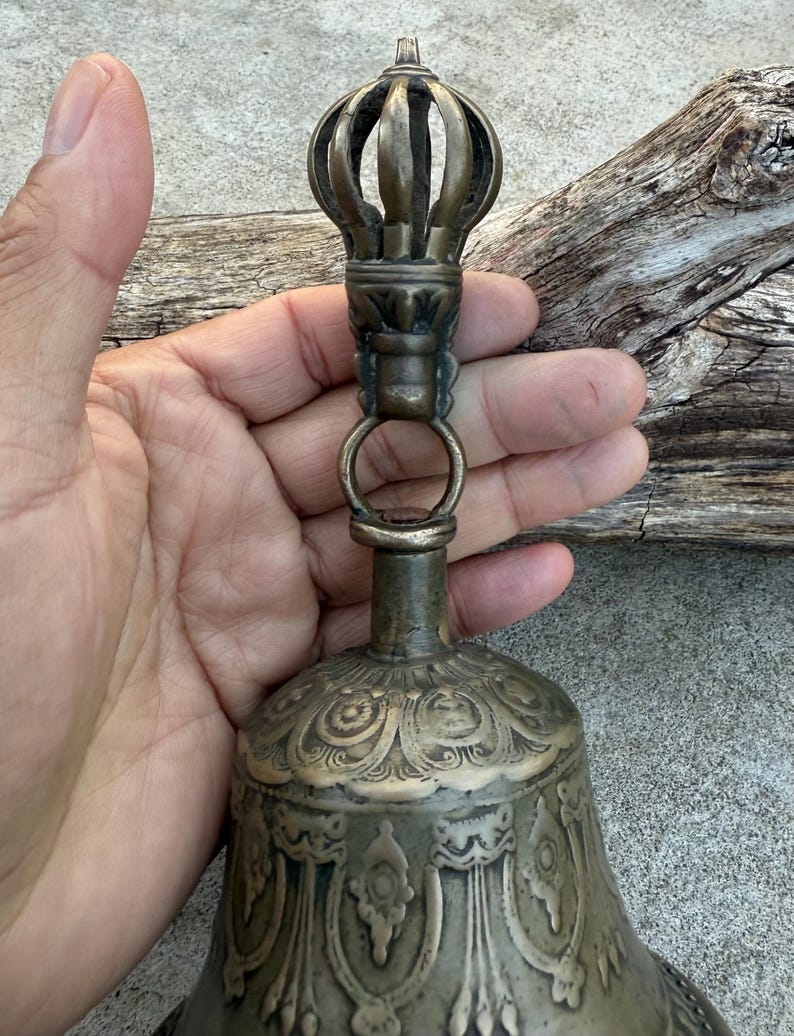 May include: A brass bell with intricate carvings and a decorative finial. The bell has a traditional design and is likely used for religious purposes.