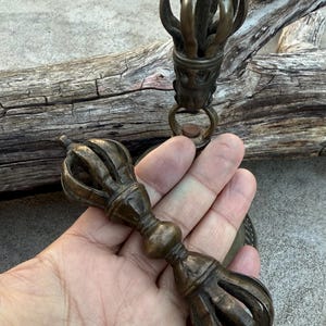 May include: A pair of antique brass Tibetan ritual bells with intricate designs. The bells are connected by a chain and have a handle with a decorative knob.
