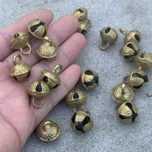 May include: A collection of 17 gold-colored jingle bells with black accents. The bells are arranged on a light gray surface.