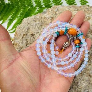 May include: A white opal mala bead necklace with orange and turquoise accents. The necklace is made of small, round beads and has a silver charm at the end.