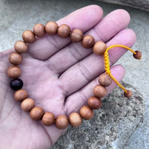 May include: A brown wooden beaded bracelet with a dark brown bead and a yellow cord.