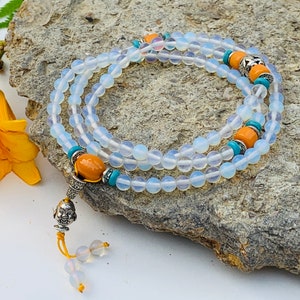 May include: A white opal mala bead necklace with turquoise and amber accents. The necklace has a silver charm at the end.