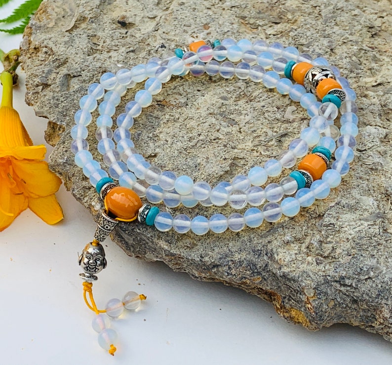 May include: A white opal mala bead necklace with turquoise and amber accents. The necklace has a silver charm at the end.