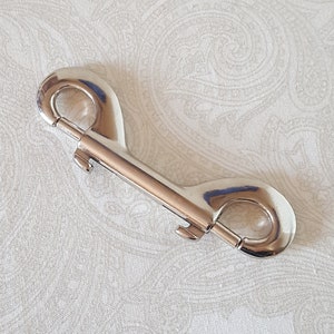 May include: Silver double ended snap hook with a swivel. The hook is made of metal and has a shiny finish.