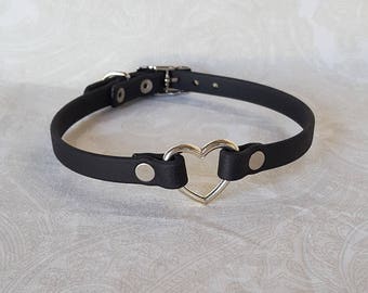 May include: A black leather choker with a silver heart-shaped ring. The choker has a buckle closure and two silver snaps.