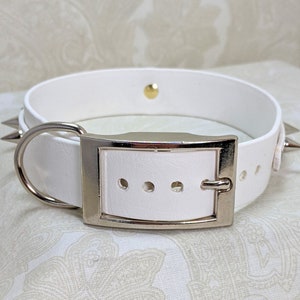 May include: White leather dog collar with silver spikes and a silver buckle. The collar has a D-ring for attaching a leash.