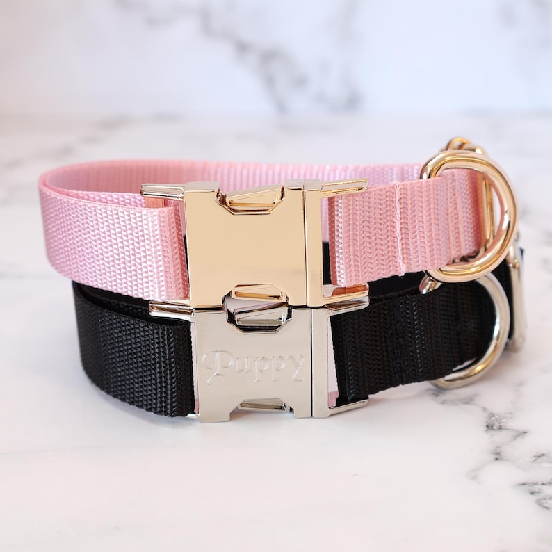 Pode incluir: Duas coleiras para c&atilde;es, uma rosa e outra preta, com fivelas prateadas e douradas. A coleira preta tem a palavra "Puppy" gravada na fivela.