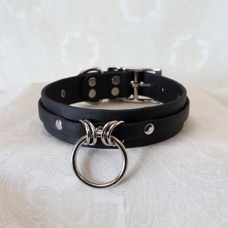 May include: Black leather choker with a silver ring and a silver buckle. The choker is double layered and has silver studs.