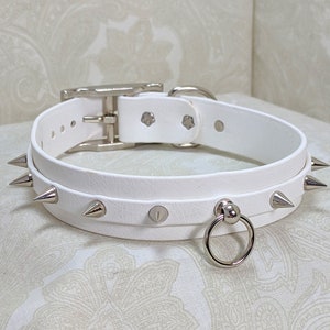 May include: White leather choker with silver spikes and a silver ring. The choker has a buckle closure.