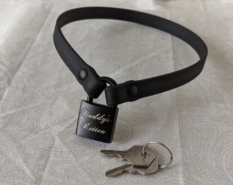 Könnte beinhalten: Schwarzer Choker mit einem schwarzen Vorhängeschloss, auf dem "Daddy's Kitten" steht, und einem silbernen Schlüssel.