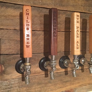 May include: Four wooden beer tap handles with different beer names engraved on them. The handles are mounted on a wooden wall. The names are "Childs Brew", "Seasonal", "Rye Pale Ale", and "Golden Ale".