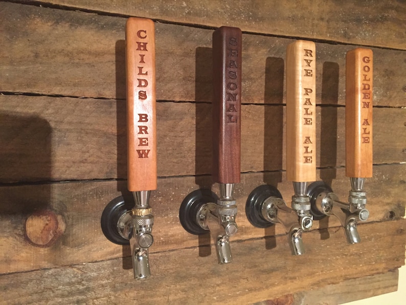 May include: Four wooden beer tap handles with different beer names engraved on them. The handles are mounted on a wooden wall. The names are "Childs Brew", "Seasonal", "Rye Pale Ale", and "Golden Ale".