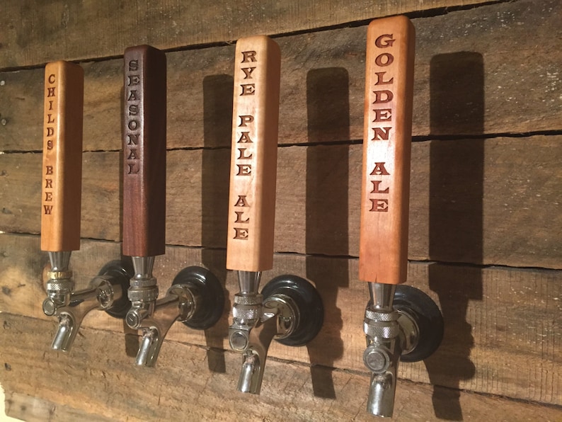 May include: Four wooden beer tap handles with different beer names engraved on them. The handles are mounted on a wooden wall. The names are "Child's Brew", "Seasonal", "Rye Pale Ale", and "Golden Ale".