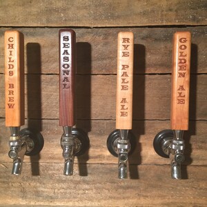 May include: Four wooden beer tap handles with different beer names engraved on them. The handles are mounted on a wooden wall. The names are "Childs Brew", "Seasonal", "Rye Pale Ale", and "Golden Ale".